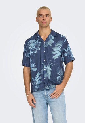 Camisa de manga corta, con botones, en tejido azul oscuro con un patrón floral en azul claro. Presenta un cuello tipo camp y un diseño de corte relajado.