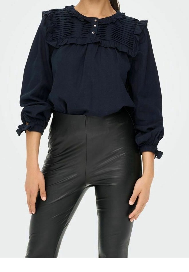 Blouse bleu marine avec col volants et panneau texturé, dotée de trois boutons. Associée à un pantalon en simili cuir noir ajusté.
