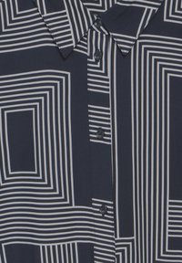 Blusa blu navy con un motivo geometrico a righe bianche, chiusura con bottoni e scollatura con colletto. Realizzata in un tessuto morbido e liscio.