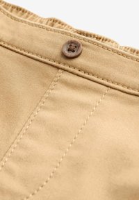 Tissu couleur khaki avec une texture lisse, présentant une fermeture à bouton et une couture contrastante le long des coutures. Vue en gros plan de la ceinture.