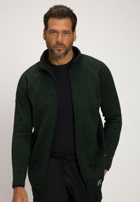 Giacca in pile verde scuro con zip frontale, colletto alto e maniche lunghe. Presenta un tessuto testurizzato e due tasche laterali.