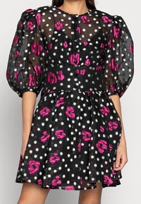 Robe noire à pois et motifs floraux roses, avec des manches bouffantes, un devant à boutons et une jupe évasée. Tissu texturé.