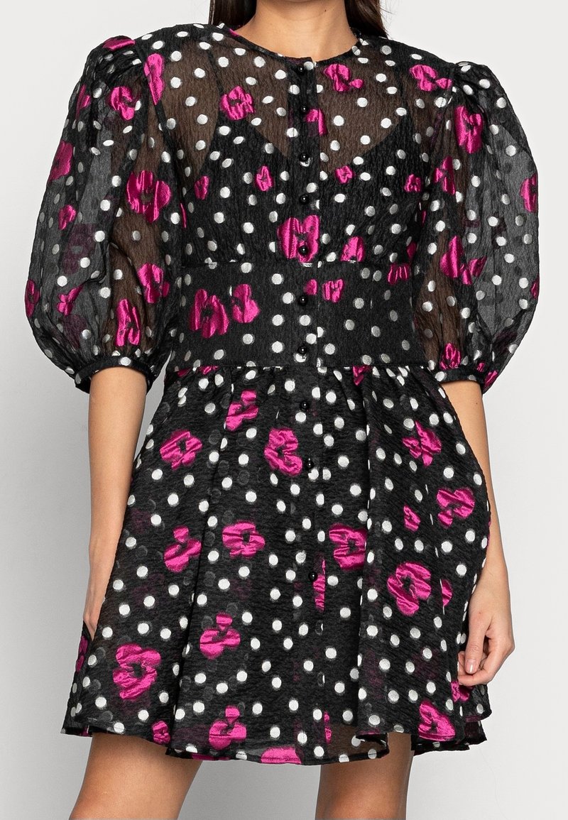 Robe noire à pois et motifs floraux roses, avec des manches bouffantes, un devant à boutons et une jupe évasée. Tissu texturé.