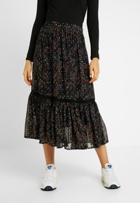 Jupe noire à motifs avec des détails floraux colorés, volants à l'ourlet, et en tissu léger et transparent. Associée à des baskets blanches.