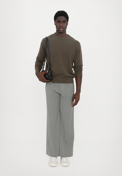 Pruun tekstuuriga sviiter, hallad laiad püksid, valged tossud ja väike must kott. Lihtne, minimalistlik disain neutraalsetes värvides.