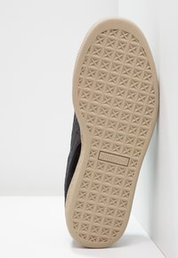 Baskets noires avec une tige texturée et une semelle extérieure en caoutchouc beige clair présentant un motif d'adhérence en forme d'étoile. Logo de la marque embossé sur la semelle.