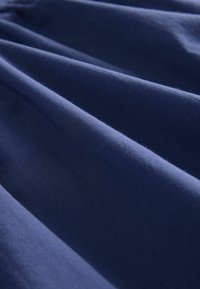 Tissu bleu marine avec une texture douce et mate, présentant de multiples plis et une surface lisse et uniforme sans motifs ni matériel visible.