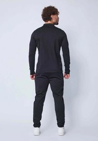 Haut à manches longues noir et pantalon assorti, fabriqués dans un matériau lisse et extensible, avec un design ajusté et une taille élastique, associés à des baskets blanches.