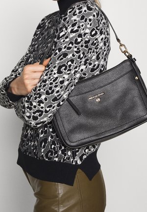 Czarna skórzana torebka o fakturowanym wykończeniu, z zamkiem błyskawicznym i złotym akcentem; noszona na wzorzystym szarej i czarnej swetrze.