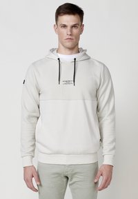 Hoodie grigio chiaro con un pannello superiore testurizzato, cappuccio standard, cordini neri e tasca frontale. Presenta il logo sul petto.