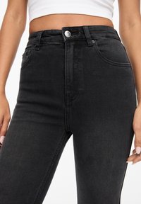 Jeans noirs taille haute en denim, avec une fermeture à bouton à l'avant, deux poches latérales et une texture lisse.