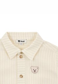 Koszula w kolorze off-white z jasnymi pionowymi paskami, z haftem w kształcie niedźwiedzia oraz dwiema guzikami z detalem logo.