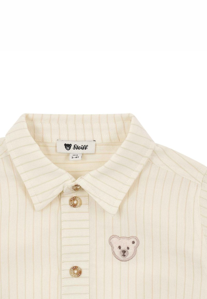Helles, off-white Hemd mit Kragen, das mit hellen vertikalen Streifen und einer Bärenstickerei sowie zwei Knöpfen mit Logodetails versehen ist.
