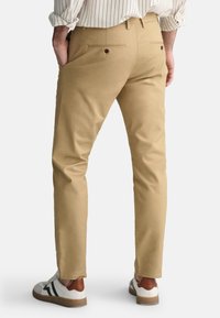 Beige chinos i bomuld med slim fit, med baglommer med knaplukninger og små sidesplitter. Samlet med hvide sneakers.
