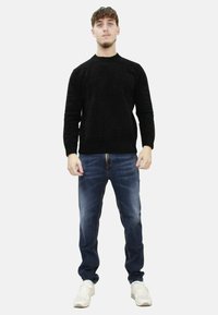 Maglione nero a maglia con scollatura rotonda, abbinato a jeans blu in denim e sneakers bianche. Il tessuto appare testurizzato e casual.