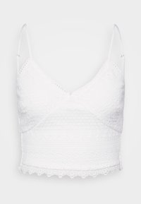 Valkoinen pitsinen bralette, jossa on säädettävät hihnat, V-mallinen kaula-aukko ja tekstuuriset kuviot. Sisältää aaltoilevan helman ja monimutkaisia brodeeraustyylejä.