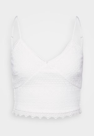White lace bralette with adjustable straps, v-neckline, and textured patterns. Features a scalloped hem and intricate embroidery details.