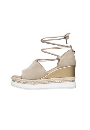 Sandale compensée avec un dessus en daim beige, un talon finition or et une semelle en caoutchouc blanche. Dotée de détails en lacets entrecroisés et d'une touche de jute.