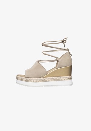 Sandale compensée avec un dessus en daim beige, un talon finition or et une semelle en caoutchouc blanche. Dotée de détails en lacets entrecroisés et d'une touche de jute.