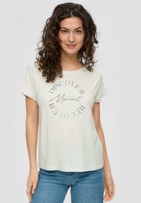 Helles Creme T-Shirt aus weichem Stoff, mit umgeschlagenen Ärmeln und Rundhalsausschnitt. Es hat ein kreisförmiges grafisches Textdesign in metallischen Farben.