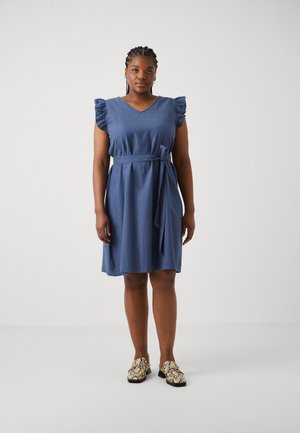 Vestido azul con mangas cortas y acampanadas, escote en V y un cinturón de lazo en la cintura. Textura suave con un corte relajado. Combinado con zapatos estampados.