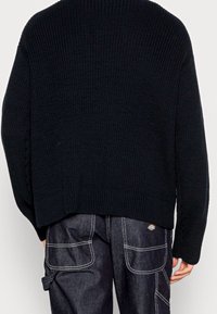 Czarny sweter dzianinowy o teksturowanym, prążkowanym wzorze, okrągłym dekolcie i obniżonych ramionach, w połączeniu z ciemnymi dżinsowymi spodniami cargo.