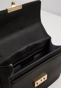 Borsa nera textured con chiusura in oro, dotata di una tasca interna con zip e un compartimento aperto per lo stoccaggio.