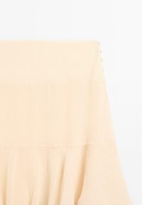 Blusa beige chiaro con tessuto texturizzato, caratterizzata da un corpino aderente e una parte inferiore svasata. Dettagli con bottoni lungo la schiena.