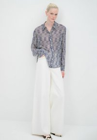 Camicia a maniche lunghe a quadretti navy e crema, abbinata a pantaloni bianchi a gamba larga. Tessuto trasparente, bottoni sulla parte frontale, stile casual.