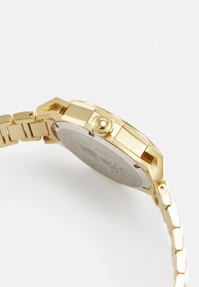 Gold metal watch with a textured back, round case, and crown. Features a linked band with polished and matte sections.