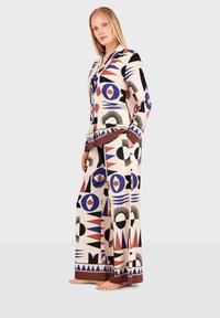 Patterned loungewear set in lightweight fabric, featuring geometric designs in red, blue, and black on a cream background, with wide pants and buttoned top.