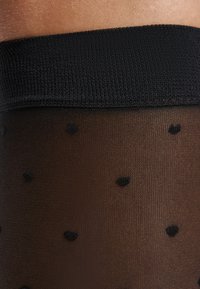 Schwarze Strumpfhosen mit einem semi-transparenten Finish, ausgestattet mit einem strukturierten Bündchen oben und einem Muster aus kleinen Herzchen.