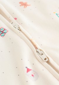 Tissu blanc à fermeture éclair arborant des motifs sur le thème de Noël, comprenant des bonshommes en pain d'épice, des bonhommes de neige et des cadeaux emballés, avec une surface texturée et de légers pois.