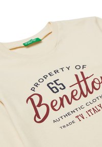 Krémové bavlněné tričko s nápisem "PROPERTY OF 65 Benetton" v námořnické a maroon barvě; kulatý výstřih a zelená etiketa na krku.