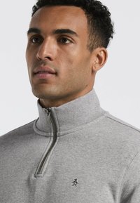 Grauer Sweatshirt mit hohem Kragen und halbem Reißverschluss. Verfügt über ein kleines Pinguin-Logo auf der Brust, mit strukturiertem Stoff und geripptem Kragen.