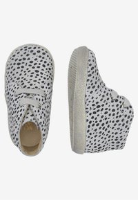 Zapatillas de lona grises con un patrón de puntos en negro, con punta redonda, sistema de cordones y suela de goma texturizada.