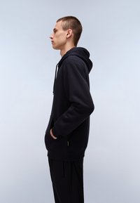 Black hoodie made of smooth fabric with a kangaroo pocket, adjustable drawstring hood, and ribbed cuffs, worn with black pants.