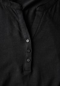 Schwarzes Henley-Shirt mit einer Knopfleiste mit vier runden Knöpfen, weichem Material und einem leicht lockeren Ausschnitt.