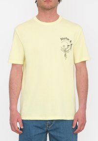 Camiseta de algodón amarilla de manga corta, con una impresión gráfica en el lado izquierdo del pecho que incluye texto y un elemento de diseño.