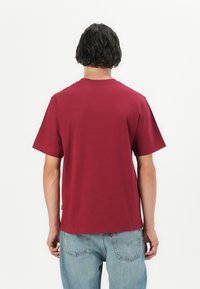 Bordeaux katoenen T-shirt met een ronde hals en korte mouwen, met een rechte zoom en een comfortabele pasvorm. Achteraanzicht weergegeven.