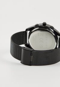 Schwarze Chronograph-Uhr mit einem Netz aus rostfreiem Stahl, glattem runden Gehäuse und einem polierten Verschluss aus rostfreiem Stahl. Auffällige Markierung auf der Rückseite.