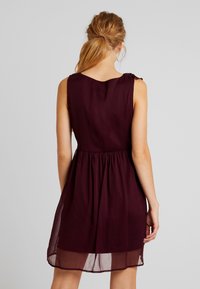 Ärmlös bordeauxklänning med en samlad midja och delikata axeldetaljer, tillverkad av lätt, halvgenomskinlig tyg.