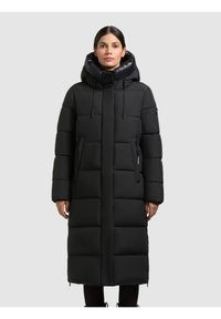 Sort lang puffjakke med hætte, der har et quilted design, frontlomme med lynlås og en lige silhuet. Glat tekstur, minimal detaljering.