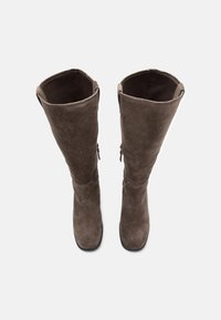 Botine maro din suede până la genunchi, cu un vârf ajustat, textură moale și o ușoară curbură în partea de sus. Dispune de un fermoar pe lateral pentru a fi ușor de purtat.