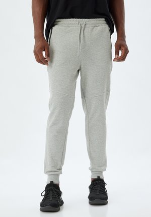 Sudadera gris de algodón con un ajuste entallado, cinturilla con cordón, bolsillos laterales y puños de canalé en los tobillos, combinada con zapatillas deportivas negras.