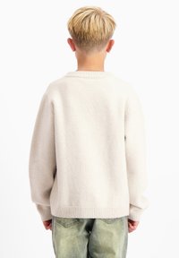 Lichtbeige trui van een zachte stof, met een ribbelkraag en -manchetten. Het ontwerp is ontspannen met een verlaagde schouder en minimale details.