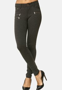 Slim-fit, mörkgrå jeans med dragkedjefickor, en slät textur och midjehög linning, tillsammans med svarta högklackade skor på en neutral bakgrund.