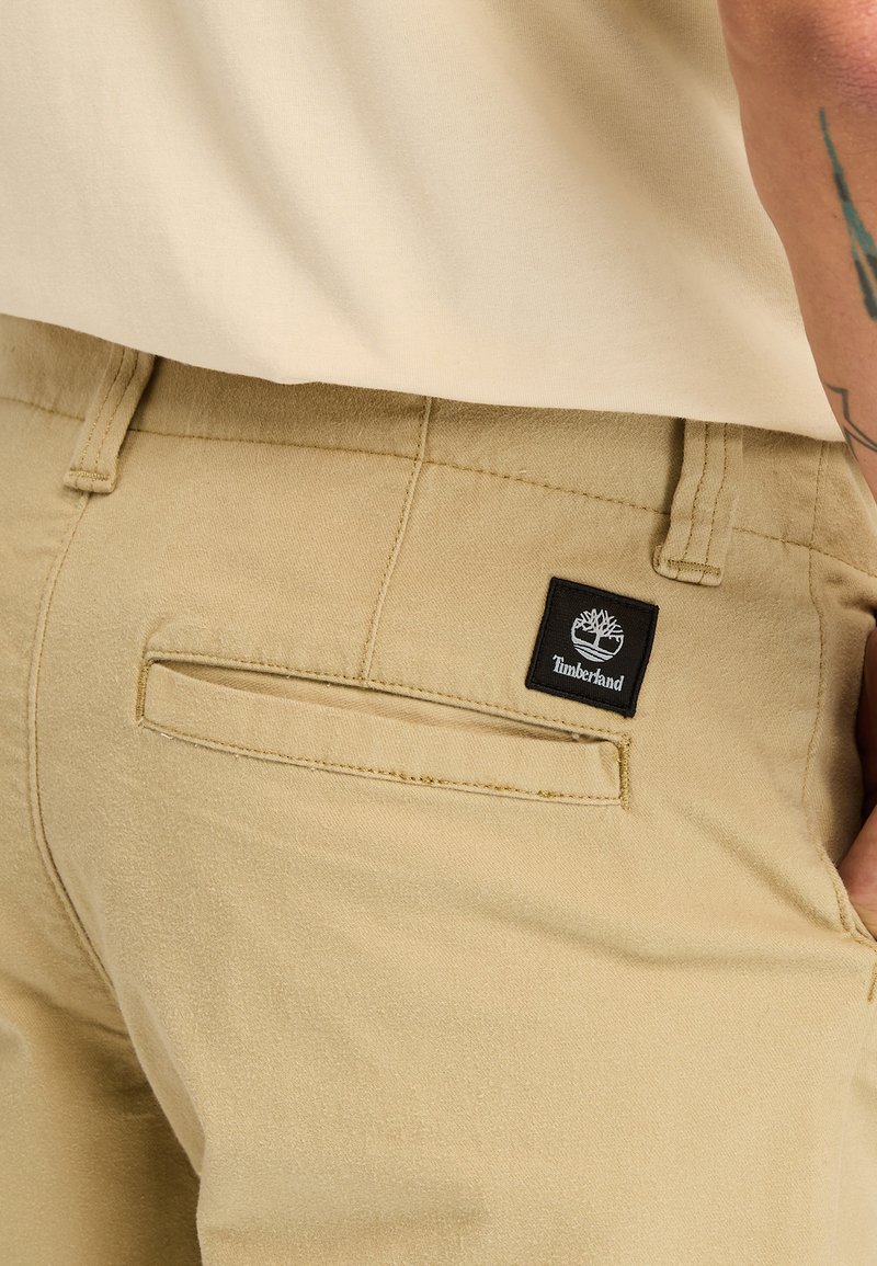 Pantaloni khaki con una trama liscia, dotati di una tasca posteriore e di una patch con il logo nero Timberland. Design semplice e classico con una vestibilità dritta.