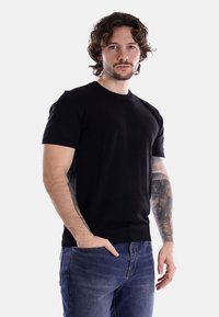 T-shirt nera a maniche corte e collo rotondo, realizzata in un tessuto a maglia liscia con una silhouette aderente. Indossata con jeans blu, senza motivi visibili.
