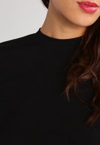 Svart ribbad topp med hög hals, med en figurnära design och slät yta, med en sömlös halsringning och utan synliga dekorationer.